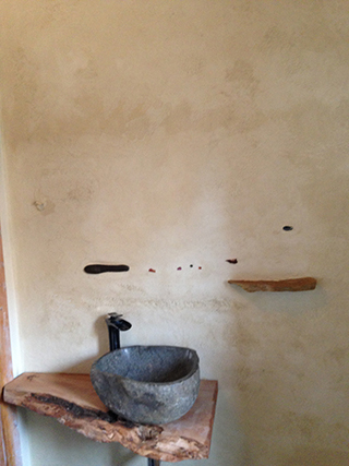 Progettazione e realizzazione di una parete con finitura in terra cruda con intrusioni e pattern superficiali in un’abitazione.